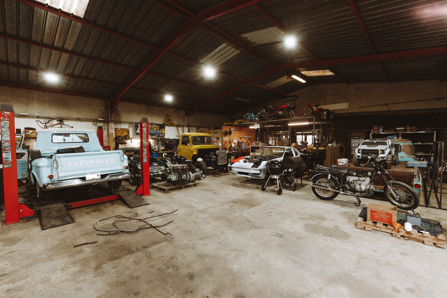 Photo du garage dans sa vie de tous les jours : On peut voir au True Love Workshop une Porsche 924 en restauration complète, une Austin Healey, un Chevrolet Apache en cours de réparation.